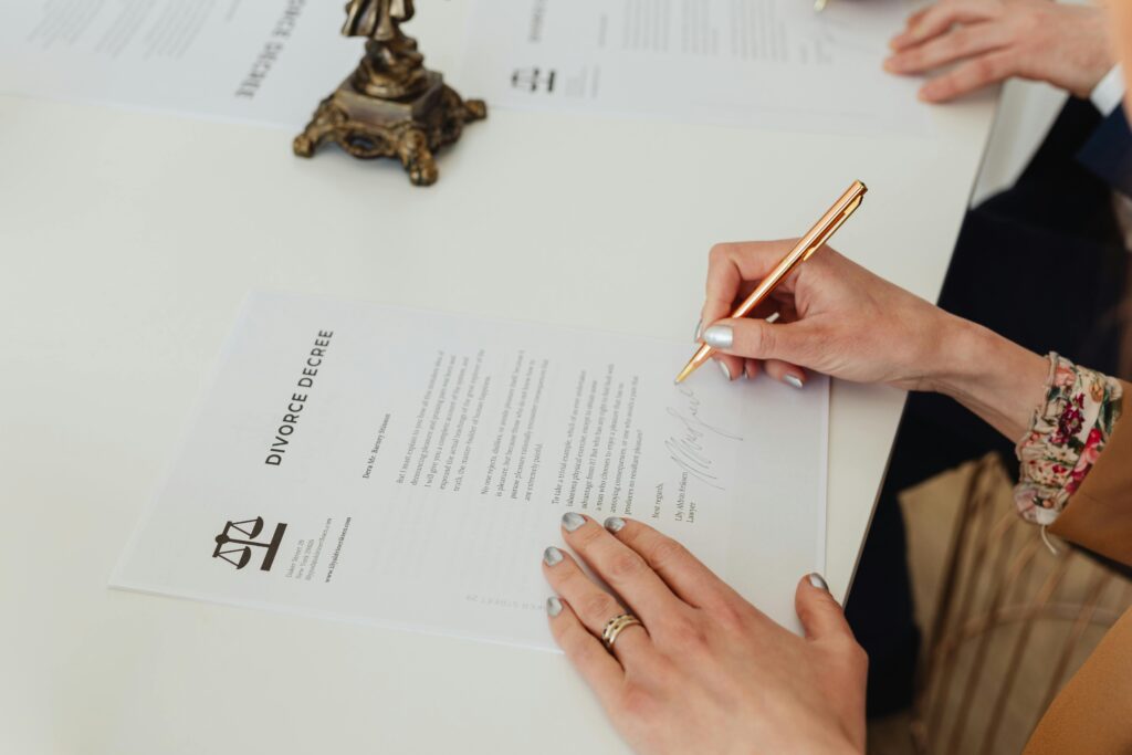 pexels-photo-7876053-7876053 Close-up of hands signing a divorce decree document on a desk, showcasing legal process.